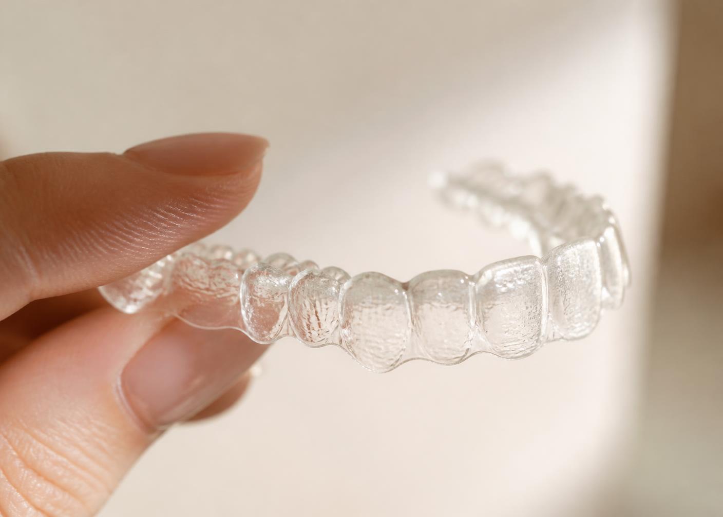 Clear Invisalign aligner held between fingertips